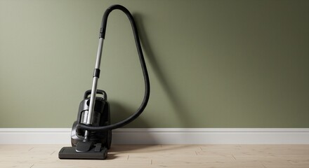 A black vacuum cleaner leans against a sage-green wall on light wood flooring A white baseboard is below