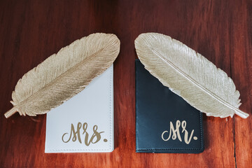 Wedding notebooks for bride and groom with golden decorative feathers on wooden table