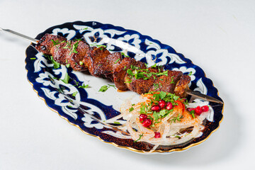 Juicy kebabs rest on a decorative plate, adorned with vibrant herbs and pomegranate seeds