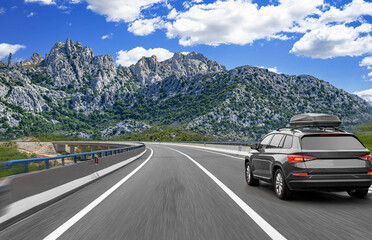 SUV with a roof box travels down a winding highway with motion blur, set against a dramatic...