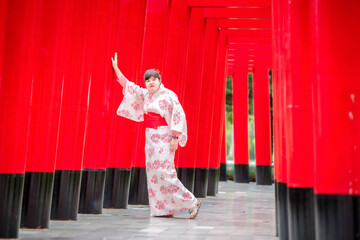  elderly Asian woman wearing a traditional Japanese yukata walks along a path with torii gates at a...