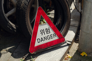 A DANGER sign in both Korean and English on a street sidewalk, surrounded by worn tires.