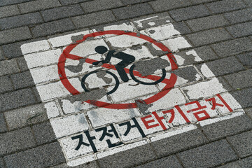 'No Cycling' sign painted on a concrete sidewalk with a red circle and Korean text.