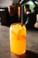 Bright orange drink filled with ice, displayed elegantly with black straws at a modern bar