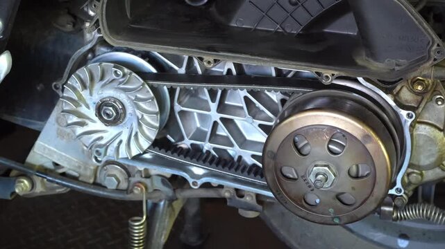 Mechanic&rsquo;s hand performing maintenance on a scooter motorcycle&rsquo;s CVT (Continuously Variable Transmission) system in a professional workshop. Ideal for illustrating concepts.