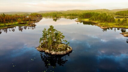 A tiny island in Norway (Mykland) with blue water around and a beautiful river in the background. The water reflects the Clouds in the sky.