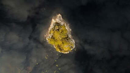 A tiny island in a lake in Norway (Mykland). Dark black water around with the clouds reflecting in the water.  