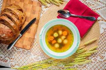 Steam wafts from a bowl of vibrant vegetable soup, with sliced bread nearby in a cozy setting