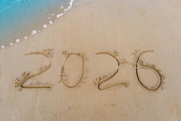 2026 numbers written in the sand. New year goal on the beach. Sea wave background.
