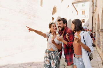 Three young tourists having fun and eating ice cream while traveling
