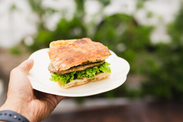 Man bringing fresh focaccia sandwiches on a white plate.