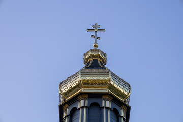 A gleaming cross decorates the top of a church dome under bright sunlight, showcasing intricate architectural details