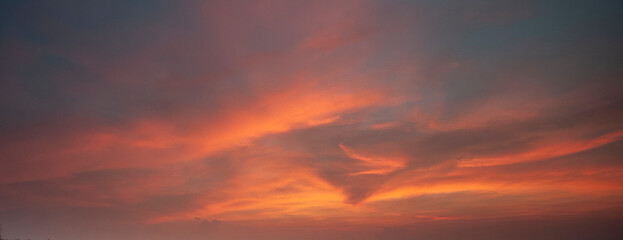 A beautiful sunset sky with dramatic and colorful clouds during twilight. The vibrant gradient of orange, purple, and blue creates a peaceful and romantic atmosphere, perfect for nature backgrounds an