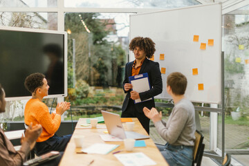 Diverse team clapping for businessman holding clipboard after successful presentation