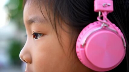 Child's profile wearing bright pink headphones, with out-of-focus foliage in the background, showing a focus on youth and technology - Powered by Adobe