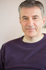 Obraz premium Middle-aged man posing in well-lit room wearing purple sweater over beige shirt with blurred plant