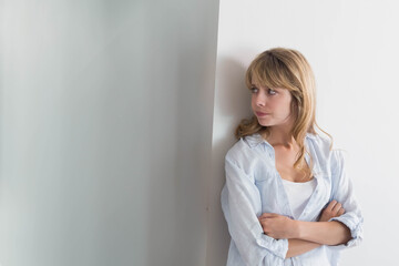 Naklejka premium Woman leaning against plain white wall in hallway with crossed arms looking left copy space