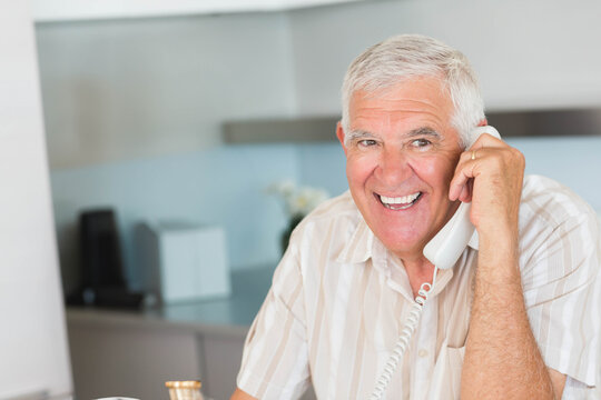 Senior man sitting at kitchen table talking on landline phone with ceramic mug, copy space