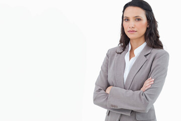 Businesswoman standing with crossed arms in studio wearing grey blazer, white shirt, copy space