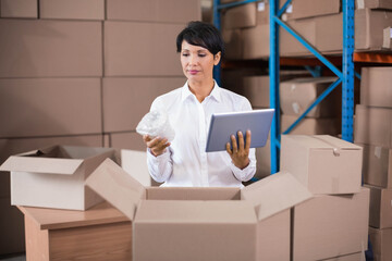 Woman holding tablet and wrapping cartons with bubble wrap at warehouse packing station