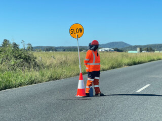Road worker stand beside a slow down traffic sign
