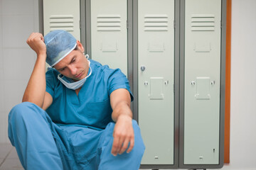 Hispanic male surgeon leaning against lockers in locker room, wearing scrubs and bouffant cap