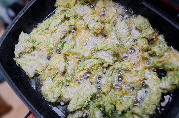 Hot oil bubbling in a black cast-iron skillet filled with vibrant green and white batter,...