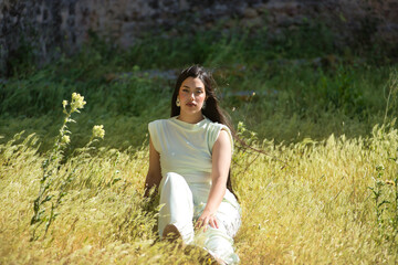 Young, pretty, brunette woman in a white dress, looking at camera, relaxed and calm, sitting among...