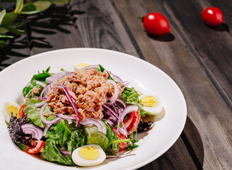 Fresh salad with tuna, eggs, and vegetables served on a wooden table