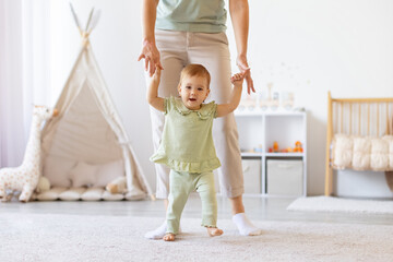 Happy baby walking with mothers help in nursery. Joyful lifestyle scene of childhood development,...