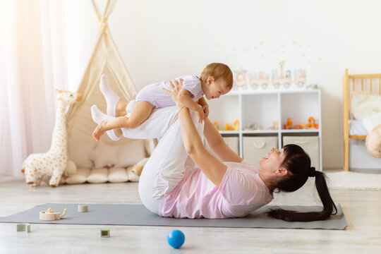 Mother lifting baby girl during yoga workout on mat at home. Family lifestyle concept of fitness, play, motherhood love, childcare, joy, balance, health and nurturing bond