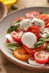 Caprese salad with sliced tomatoes, mozzarella, basil, olive oil close up on brown textured background
