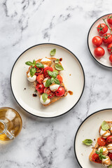 Caprese sandwich or toast with mozzarrella balls, cherry tomatoes, olive oil and fresh basil leaves top view. Healthy vegetarian breakfast, snack or lunch. White marble background
