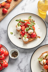 Caprese sandwich or toast with mozzarrella balls, cherry tomatoes, olive oil, pepper and fresh basil leaves. Healthy vegetarian breakfast, snack or lunch. White marble background