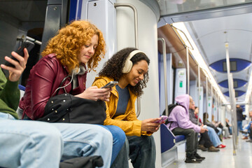 Young women using smartphones on subway train during commute