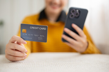 Close up of woman's hands holding phone and showing a credit card while sitting at table in cafe.