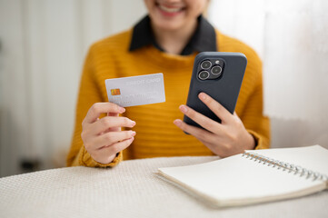 Close up of a young woman holding phone showing and looking at credit card while sitting at table.