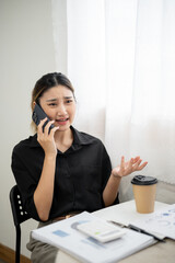 Upset asian businesswoman office worker holding and talking on phone aside laptop at working table