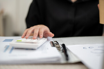 Fototapeta premium Close up of businesswoman or office worker's hand using a calculator over documents at working table