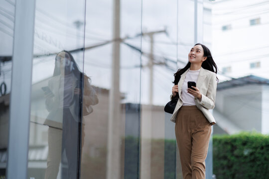 Smiling businesswoman walking near office building holding smartphone