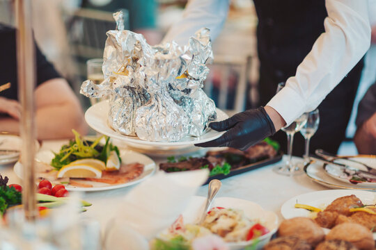 Served with elegance, a waiter's presentation of gourmet dishes at a festive gathering during a sunny afternoon in an upscale dining venue, delivering a culinary experience to guests