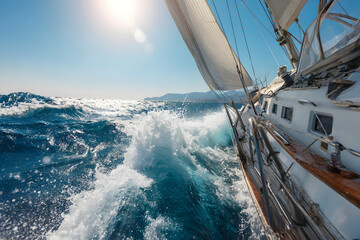 White yacht sailing on a clear sunny day. Close-up view from the deck to the bow and sails. Waves and water splashes.