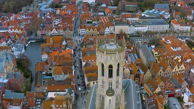 4K drone close-up of the Belfry of Bruges rising over red rooftops, canal and crowds in the UNESCO old town - an iconic medieval Belgium cityscape in cinematic detail.
