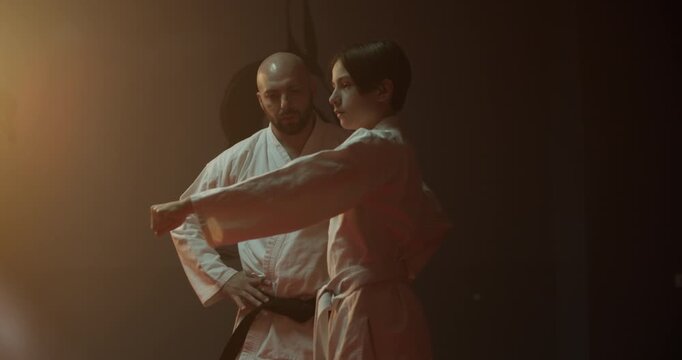 Karate master controls young practitioner training strikes in gym