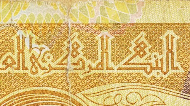 Macro pan along an Iraqi banknote showing Arabic calligraphy for the Central Bank with gold guilloche and aged paper texture