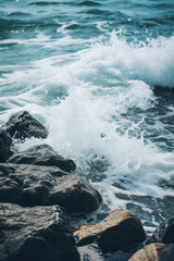 Fototapeta premium Powerful ocean waves crash onto dark textured rocks at the shoreline creating white foam and spray