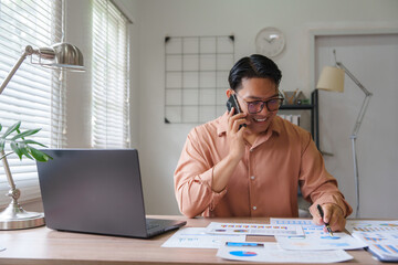 Asian businessman talking on phone and analyzing charts in home office