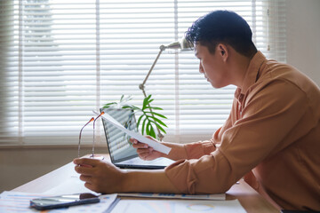Asian businessman working from home reading documents and using laptop