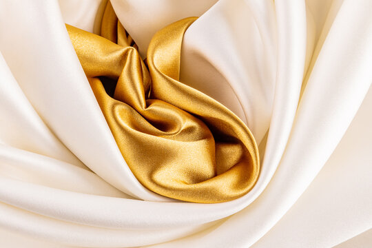 Satin fabric background with ivory and gold folds
