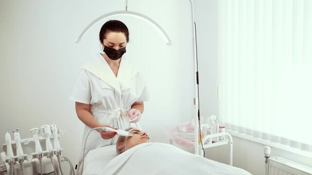 Cosmetologist beautician using facial skin scrubber during treatment at skin care clinic. Female specialist focusing on gentle exfoliation and deep pore cleansing. Lady beautician providing